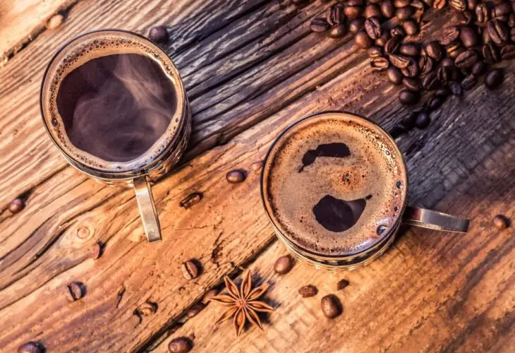 Two cups of coffee and scattered beans on a rustic table, representing the sensory quality preserved through supercritical CO₂ caffeine extraction.