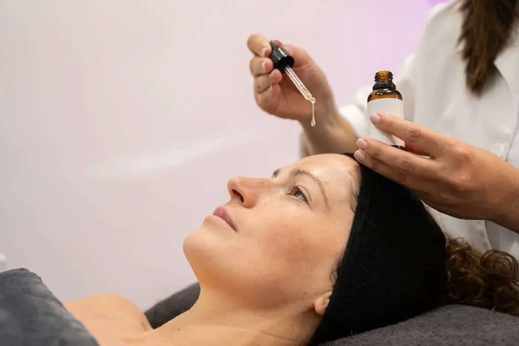 Woman receiving a facial skincare treatment with a dropper applying encapsulated retinol serum, performed by a professional in a cosmetic clinic.
